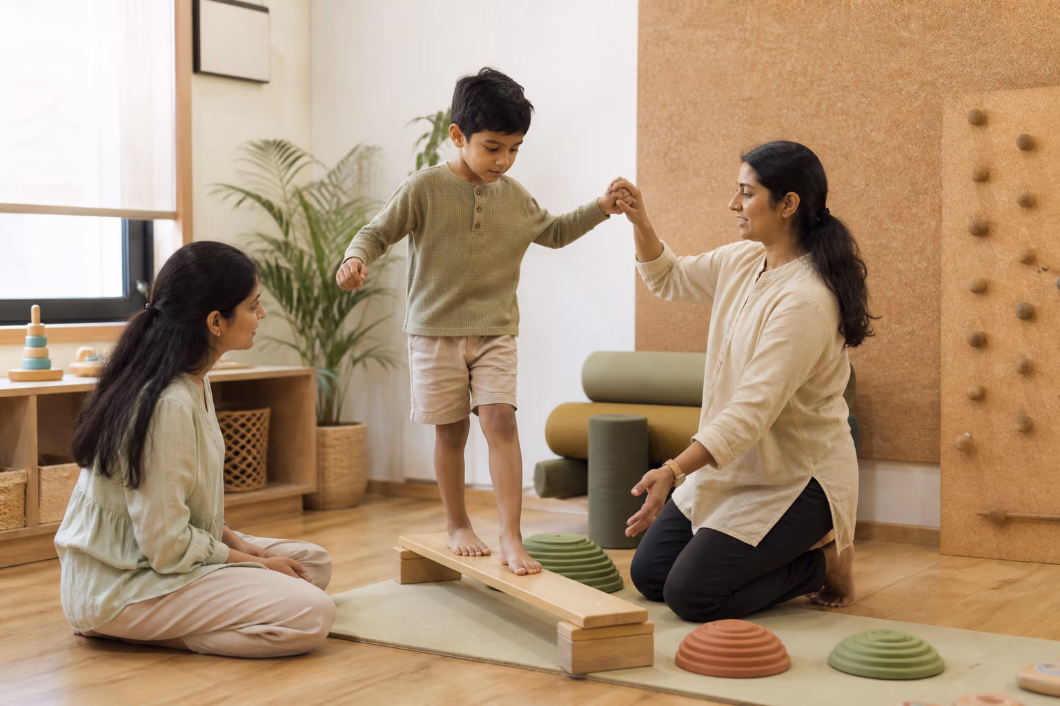A child completing a balance activity with a developmental therapist while a parent joins in.