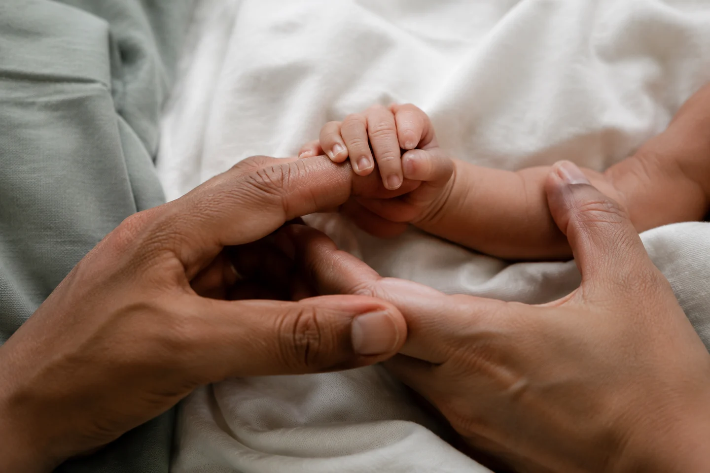 A newborn’s hand resting in the hand of a parent
